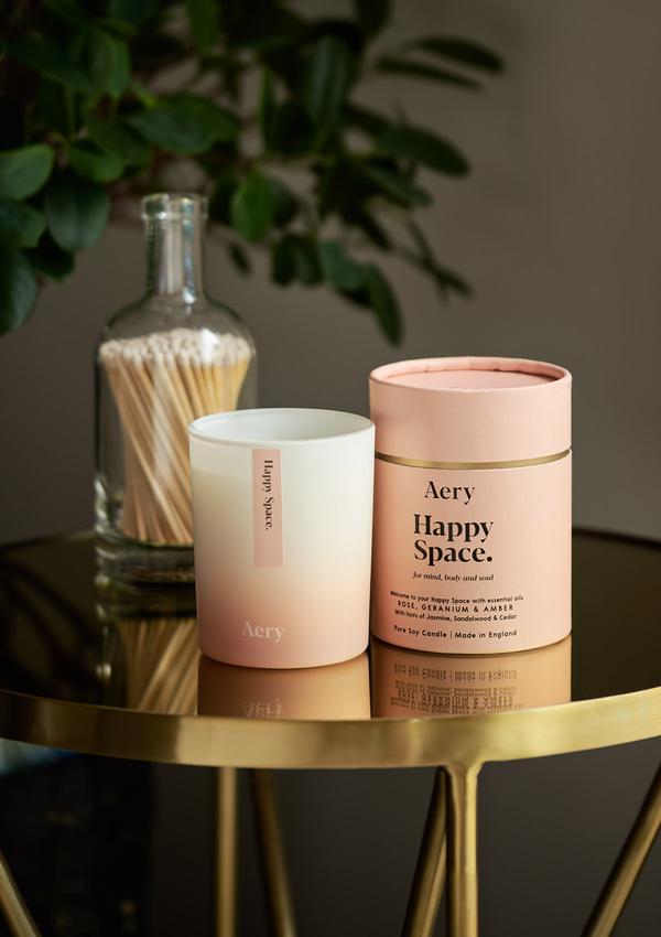 Doftljuset Happy Space från Aery Living som luktar Rose, Geranium och Amber. Produkten står på bord i guld.