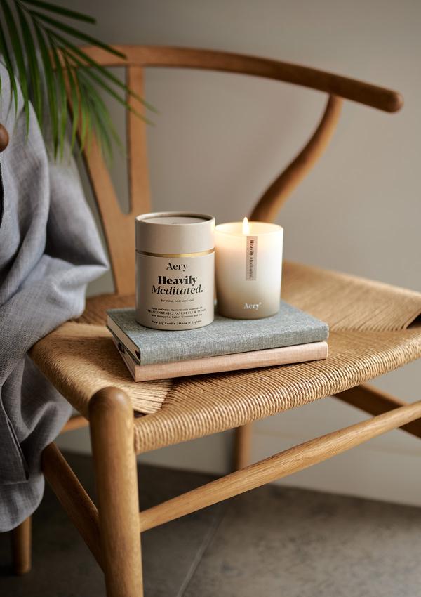 Doftljuset Heavily Meditated från Aery Living. Doftljuset luktar Patchouli, rökelse och timjan. Produkter står på två böcker på en designer stol i trä. 