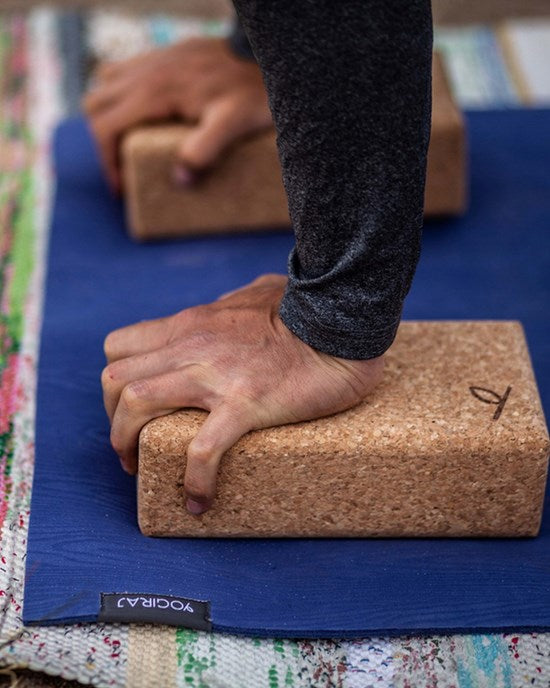 Miljöbild på en person som står i armhävningsställning med händerna på två yogablock på en blå yogamatta.